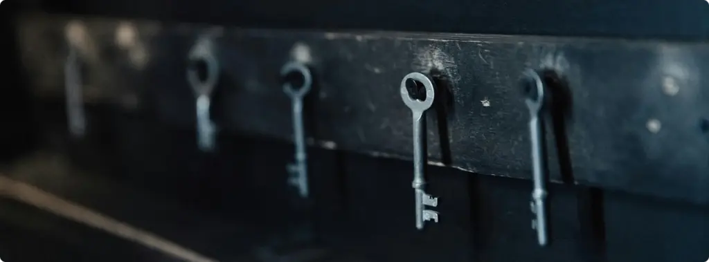 Een reeks oude metalen sleutels hangt aan spijkers tegen een zwarte achtergrond