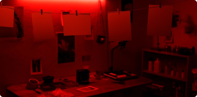 De foto's drogen aan een touw in een donkere kamer waar de film wordt ontwikkeld, met een felrode lamp boven de werktafel.