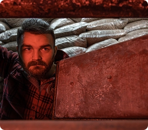 Een man met een baard kijkt in de ketel, die van binnenuit door rood licht wordt verlicht, met zakken op de achtergrond.